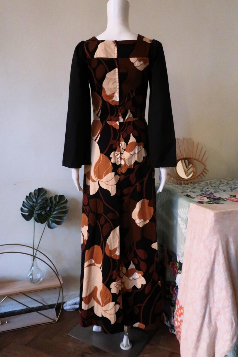 May include: A long black and brown floral maxi dress with long bell sleeves. The dress has a square neckline and a fitted bodice.