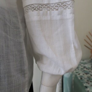 May include: White linen blouse with a lace trim on the sleeves. The sleeves are gathered at the wrist.