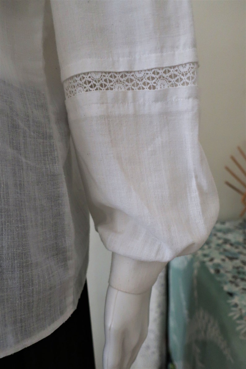 May include: White linen blouse with a lace trim on the sleeves. The sleeves are gathered at the wrist.