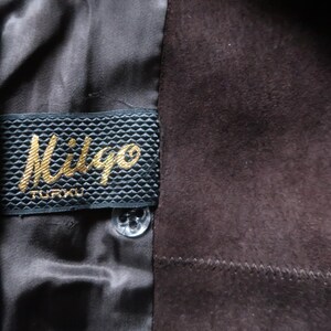 May include: Close-up of a brown suede jacket with a black label that reads "Miligo TURKU".