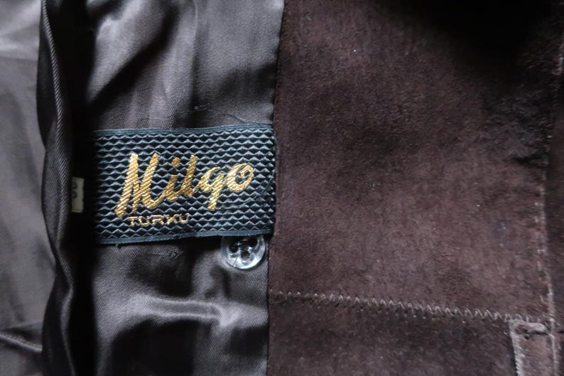 May include: Close-up of a brown suede jacket with a black label that reads "Miligo TURKU".