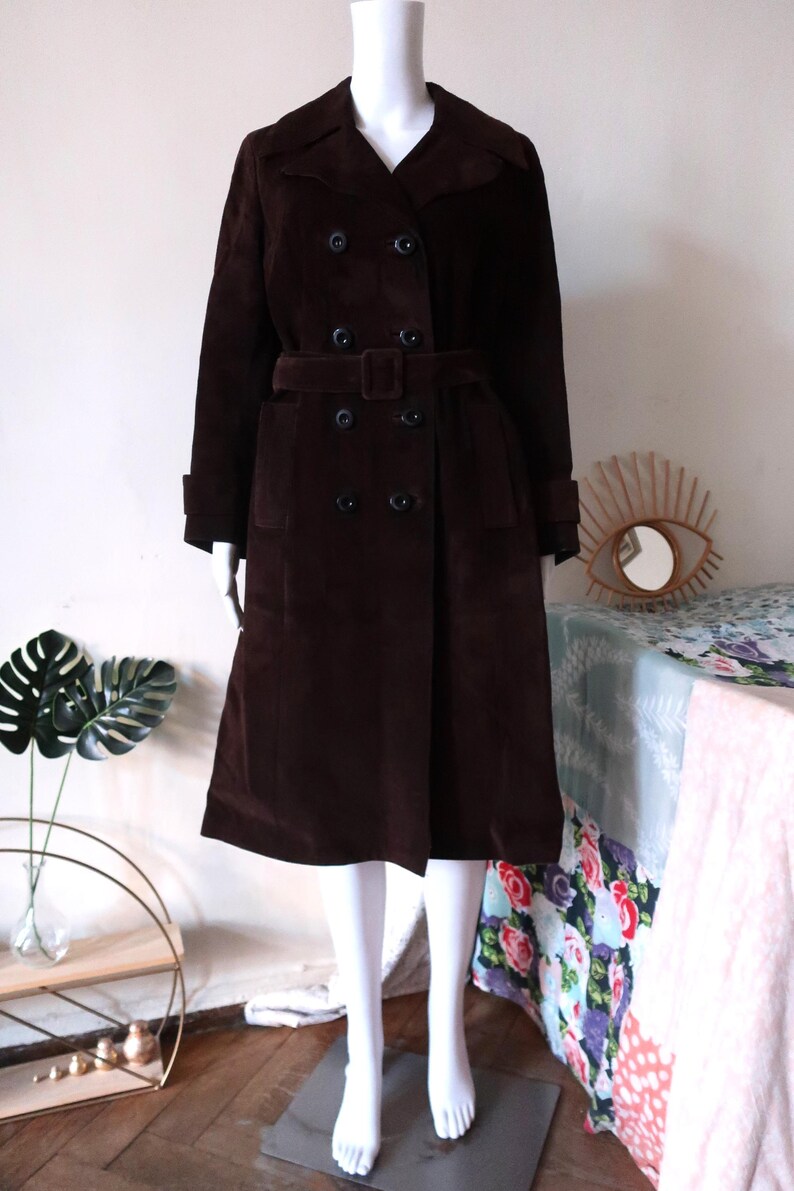 May include: A brown corduroy trench coat with a double breasted closure, a belt, and two pockets. The coat is on a white mannequin.
