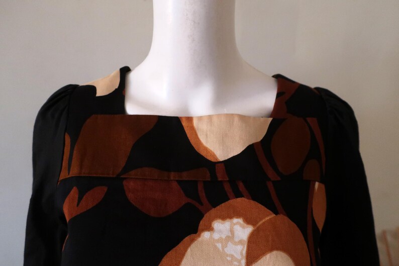 May include: A black long-sleeved dress with a square neckline and a brown and beige abstract floral print.