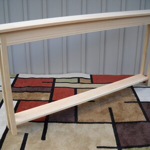 May include: A natural wood console table with a simple design. The table has a rectangular top and a single shelf. The table is made of unfinished wood and is ready to be stained or painted.