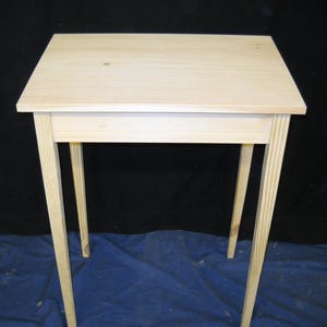 May include: A simple, unfinished wooden table with four legs and a single shelf. The table is made of light-colored wood and has a natural finish.