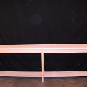 May include: A long, unfinished wooden console table with a lower shelf. The table has a light, natural wood color and a simple, rectangular design. The table is approximately 72 inches long.