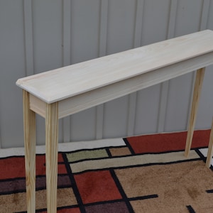 May include: A light wood console table with a rectangular top and four slender legs. The table is unfinished and has a natural wood grain.