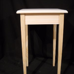 May include: A simple, unfinished wooden end table with a white top and four legs. The table is made of pine wood and has a natural wood grain.