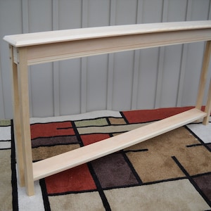 May include: A natural wood console table with a rectangular top and a lower shelf. The table is made of unfinished wood and has a simple, modern design.