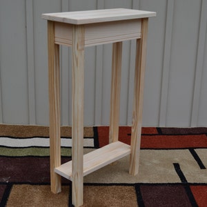 May include: A simple, unfinished wooden table with a shelf. The table is made of light-colored wood and has a rectangular top and a single shelf.