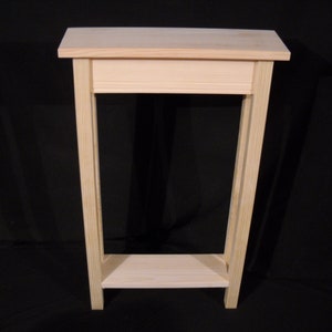 May include: A simple, unfinished wooden end table with a shelf. The table is made of light-colored wood and has a rectangular top and a single shelf.