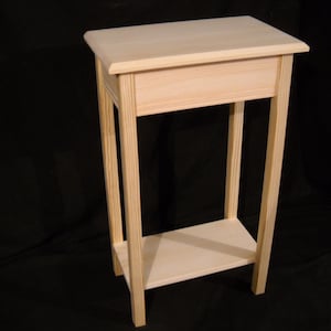 May include: A simple, unfinished wooden end table with a shelf. The table is made of light-colored wood and has a rectangular top and a single shelf.