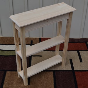 May include: A simple, unfinished wooden console table with two shelves. The table is made of pine wood and has a natural wood finish. It is 30 inches tall and 16 inches wide.