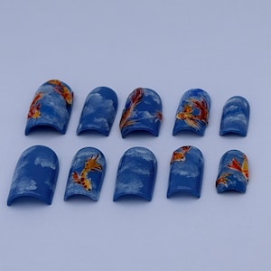 May include: A set of ten blue press-on nails with a glossy finish. Each nail features a design of white clouds and orange koi fish. The nails are arranged on a white surface, showcasing the detailed artwork.
