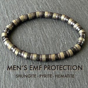 Puede incluir: Una pulsera circular compuesta por cuentas planas en forma de disco que alternan entre dorado metálico y negro pulido. El texto debajo de la pulsera dice: MEN'S EMF PROTECTION SHUNGITE - PYRITE - HEMATITE. Las cuentas siguen un patrón repetitivo.