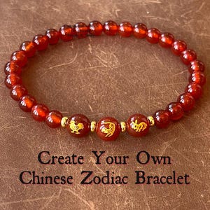 May include: Red beaded bracelet with gold accents and Chinese zodiac symbols. The bracelet features the text "Create Your Own Chinese Zodiac Bracelet". The beads are a deep red colour.