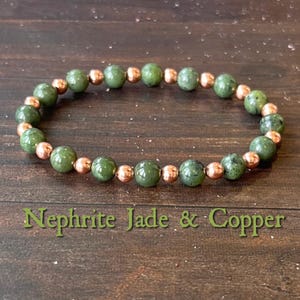 May include: A Nephrite Jade and copper bead bracelet. The bracelet features round, polished green jade beads interspersed with smaller, copper-colored beads. The text "Nephrite Jade & Copper" is displayed in green.