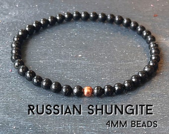 May include: A beaded bracelet featuring small, round, black Russian Shungite beads measuring 4mm in diameter, accented with a single metallic copper-colored bead. The text RUSSIAN SHUNGITE 4MM BEADS is clearly visible below the bracelet.