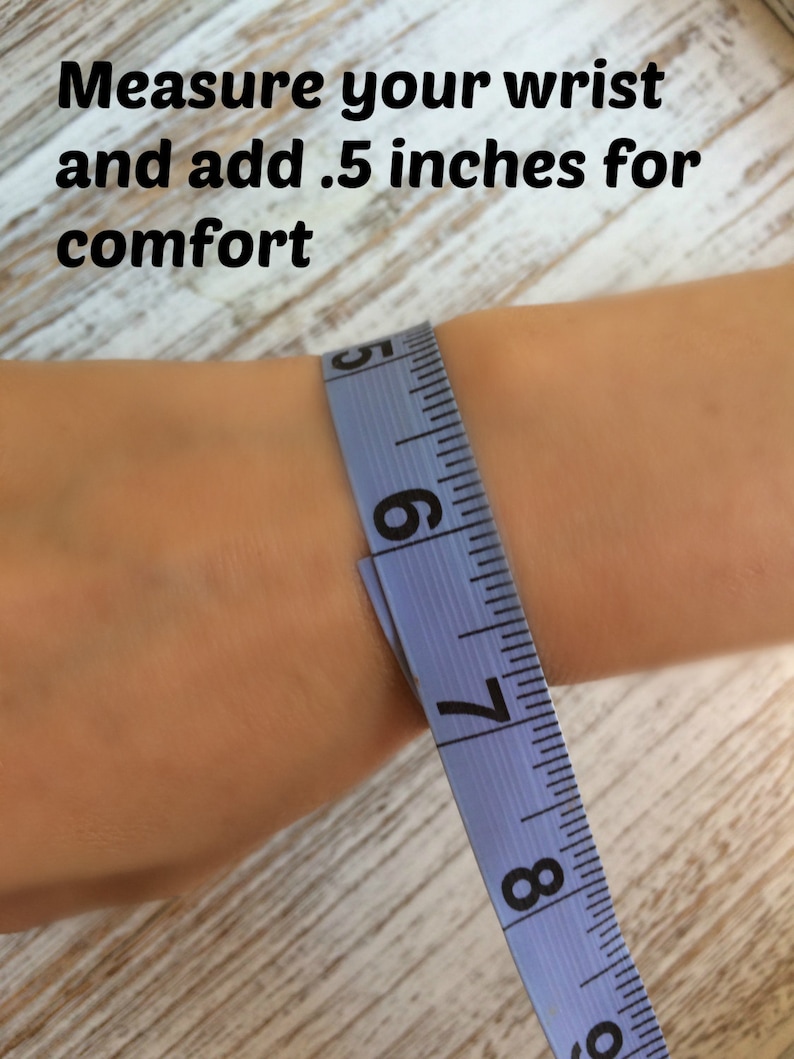 Puede incluir: Primer plano de una mu&ntilde;eca medida con una cinta m&eacute;trica azul. El texto dice: "Mide tu mu&ntilde;eca y a&ntilde;ade 1,3 cm para mayor comodidad". La escala est&aacute; en pulgadas.