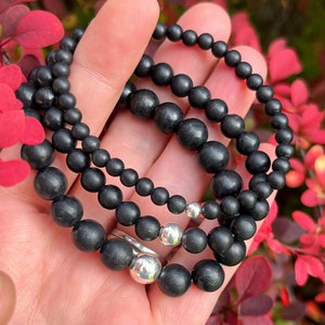 May include: Three black beaded bracelets with silver accents. The bracelets are stacked on top of each other and are being held in a hand.