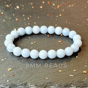 Puede incluir: Una pulsera de cuentas azul claro. La pulsera est&aacute; hecha de cuentas redondas de 8 mm. Las cuentas est&aacute;n ensartadas para formar una forma circular. La pulsera se muestra sobre una superficie oscura.