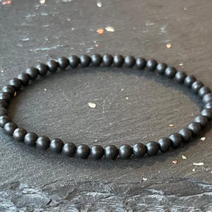 Puede incluir: Un brazalete negro hecho de cuentas redondas y mate.