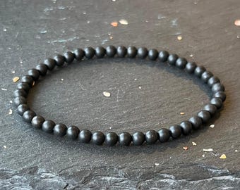 Puede incluir: Un brazalete negro hecho de cuentas redondas y mate.