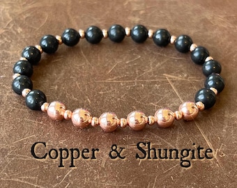 May include: A beaded bracelet featuring alternating round black shungite beads and metallic copper-colored beads. The bracelet is arranged in a circular pattern with the text Copper & Shungite printed in black below the jewelry piece.