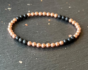 May include: A bracelet made of black and rose gold beads. The bracelet is made of small, round beads that are strung together on a thin cord.
