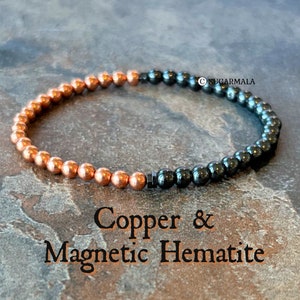 May include: A bracelet made of copper and magnetic hematite beads. The bracelet has copper beads on one side and black beads on the other. The text "Copper & Magnetic Hematite" is displayed below the bracelet. The beads are approximately 0.4 cm in diameter.