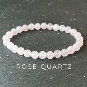May include: A pink rose quartz bracelet with round beads. The bracelet is on a dark gray background.  Rose Quartz.