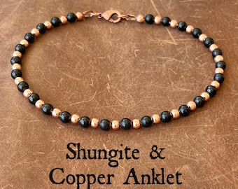 May include: An anklet featuring alternating black shungite beads and metallic copper beads arranged in a circular pattern. The piece includes a copper lobster claw clasp and is displayed above the text Shungite & Copper Anklet.