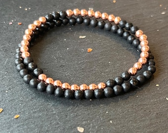 May include: A double-strand bracelet with black and rose gold beads. The bracelet is made of matte black and shiny rose gold beads.