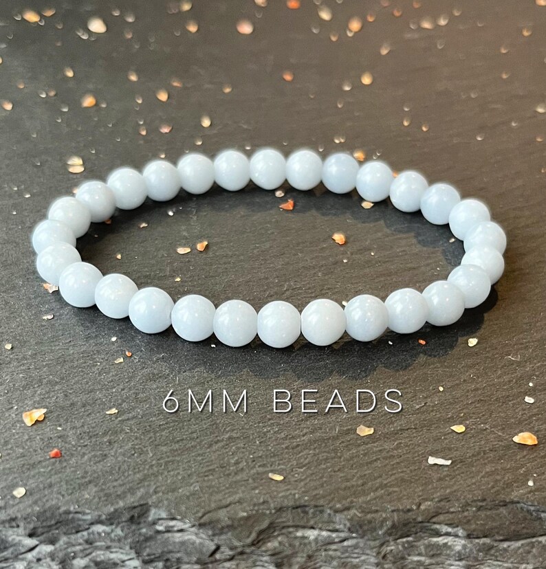 Puede incluir: Una pulsera de cuentas azul claro con cuentas de 6 mm. La pulsera est&aacute; hecha de cuentas redondas y lisas y se muestra sobre una superficie oscura y texturizada. El texto "6MM BEADS" es visible debajo.