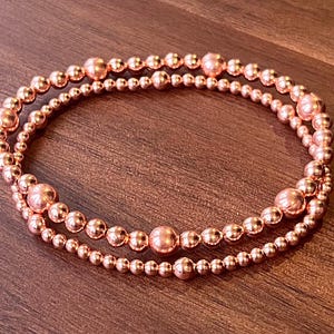 May include: A double-strand bracelet made of rose gold beads. The bracelet is made of small, round beads that are evenly spaced.