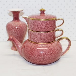 Peut inclure: Un service à thé et un vase vintage avec une finition marron mouchetée et des bordures dorées. L'ensemble comprend une théière, deux tasses empilées et un grand vase. La théière a un bec et une anse incurvés.