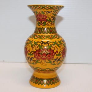 May include: A yellow ceramic vase with a floral design. The vase has a wide base and a narrow neck. The floral design is in shades of red, green, and gold.