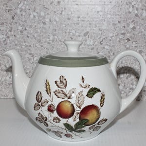 May include: White teapot with a green band around the top. The teapot has a floral design with brown leaves and red and yellow apples.