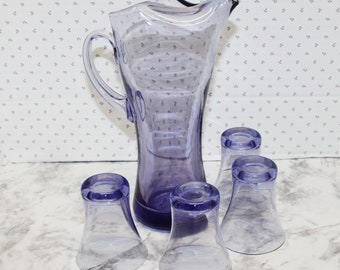 May include: A set of five amethyst-colored glass pitcher and glasses. The pitcher has a wide mouth and a handle. The glasses are short and have a wide base.