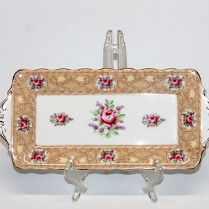 May include: A rectangular porcelain serving tray with a gold and brown floral pattern. The tray has a scalloped edge and two handles. The floral pattern features pink roses and green leaves.