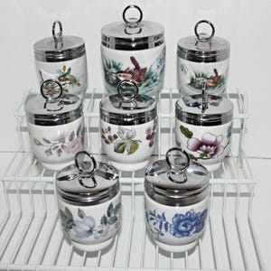 May include: Set of eight white ceramic egg coddlers with floral and bird designs. Each coddler has a silver lid with a handle.