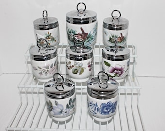 May include: Set of eight white ceramic egg coddlers with floral and bird designs. Each coddler has a silver lid with a handle.