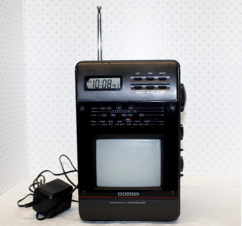 May include: A black and silver Citizen brand portable television and radio with a built-in clock displaying 10:08. The television is a black and white model with an antenna.