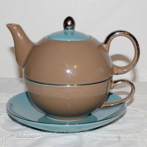 May include: A brown and blue teapot with a matching cup and saucer. The teapot has a silver lid knob and a silver handle. The cup and saucer have a silver rim.