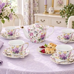 May include: A porcelain tea set comprising a teapot and four teacups with matching saucers, all decorated with a colourful floral and butterfly pattern. Each piece has gold-toned trim. Four silver-toned spoons are placed on the saucers.