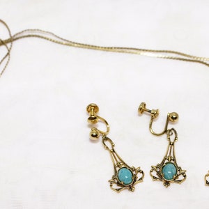 May include: A vintage jewelry set featuring a gold-toned necklace and matching earrings. The necklace and earrings have a filigree design with a turquoise-colored stone in the center. The earrings are clip-on style.