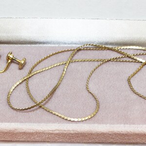 May include: A vintage jewelry set featuring gold-toned metal. The set includes a necklace with a pendant and a pair of clip-on earrings. Each piece has a light blue oval stone. The jewelry is displayed in a pink velvet-lined box.
