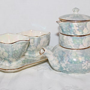 May include: A vintage tea set with a blue and white floral pattern. The set includes a teapot, two cups, and a saucer. The teapot has a lid and a handle. The cups have a scalloped edge. The saucer is rectangular.