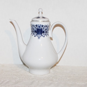 May include: White porcelain coffee pot with a blue and white floral design. The pot has a lid with a gold trim.