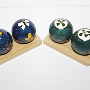 May include: Two sets of blue and green Chinese meditation balls with butterfly and clover designs on a wooden base.